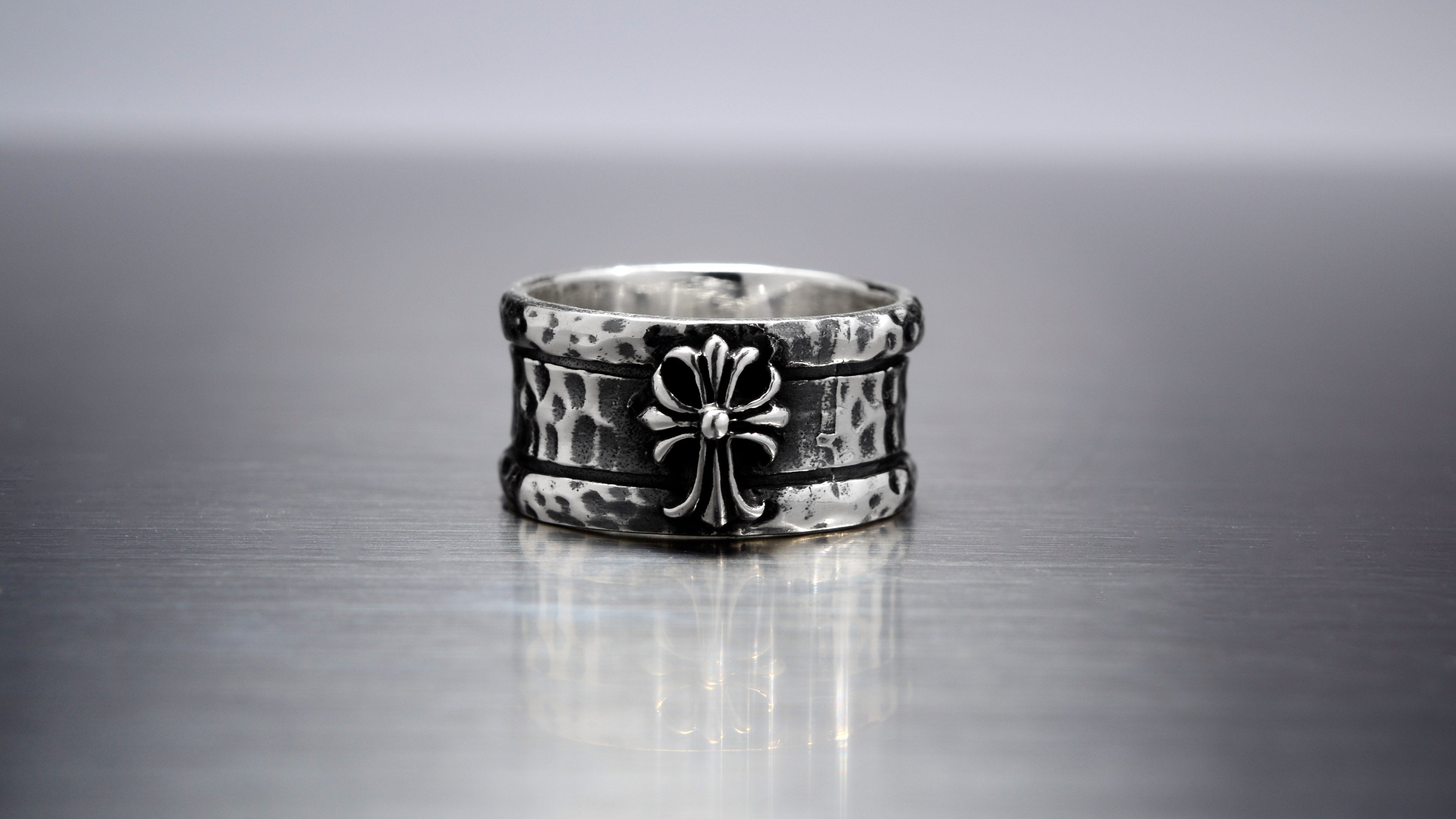 Noctain Aegis Ring aus hochwertigem 925 Sterling Silber Noctain Opium Style, massiver Gothic Herrenring mit poliertem Lilienkreuz und dunkel oxidierter gehämmerter Oberfläche auf metallischem Hintergrund.